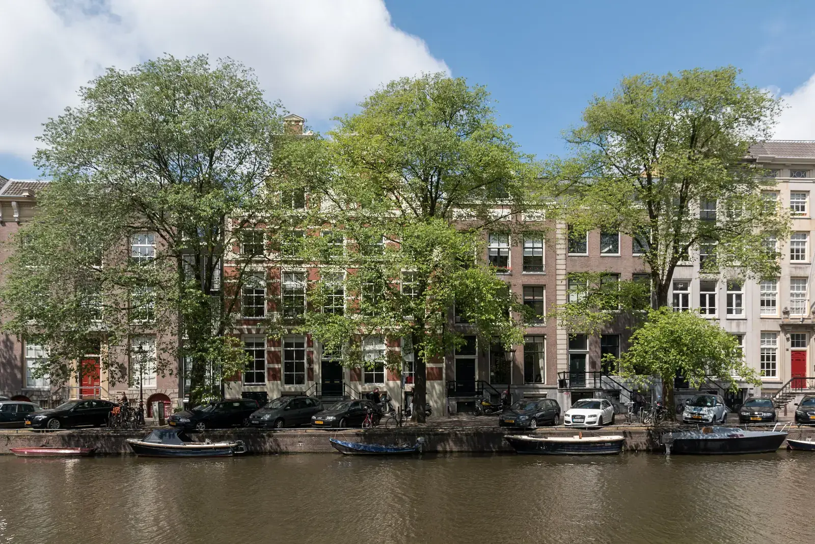 Grachtenpanden aan het Singel in Amsterdam, met volgroeide straatbomen langs de kade en boten in het water.