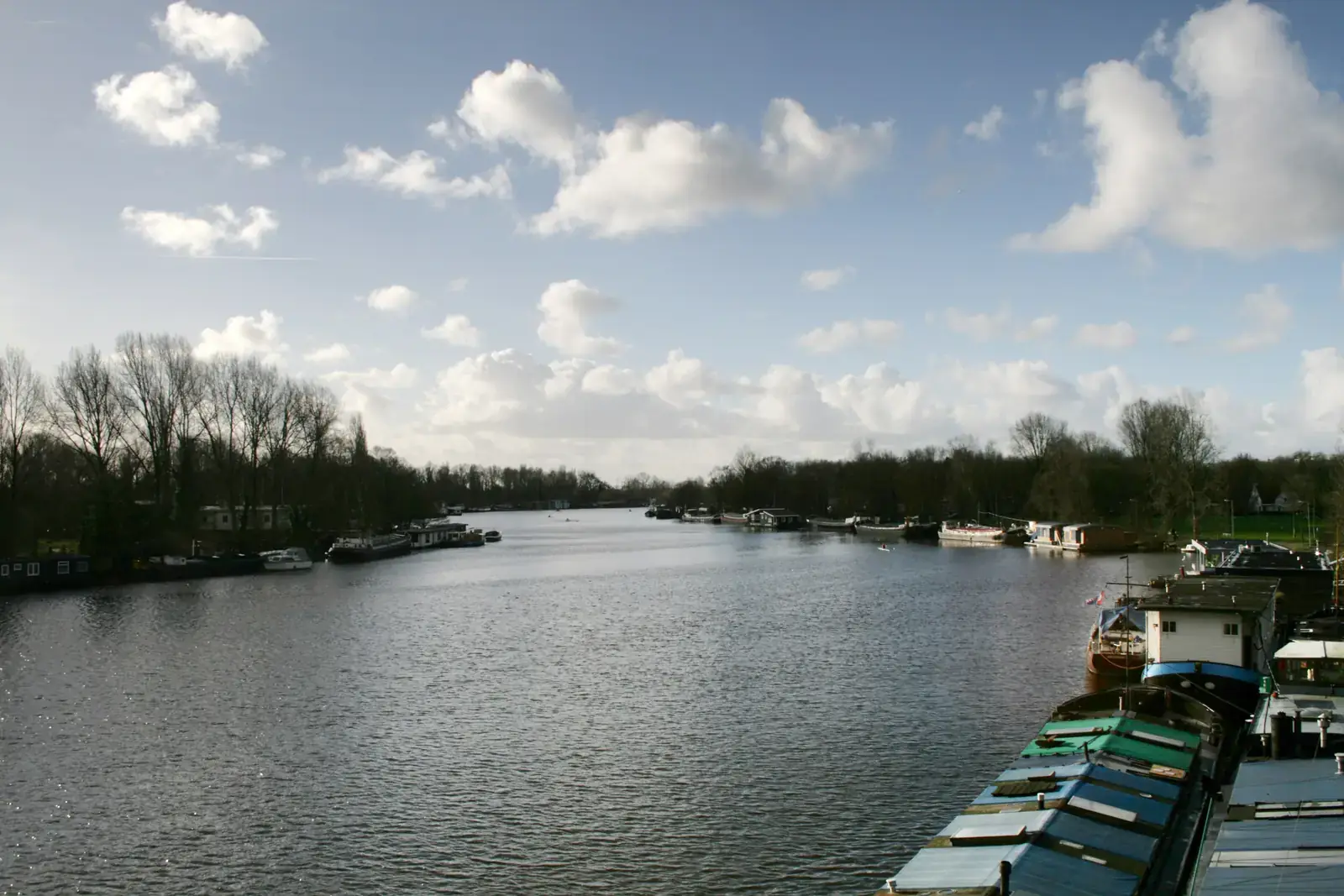 De Amstel in Amsterdam gezien vanaf de Utrechtsebrug, met woonboten langs beide oevers en kale bomen onder een bewolkte winterlucht.